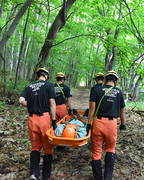 森の中で訓練をする山岳救助隊の様子、担架で救助者を搬送している様子