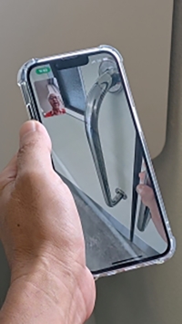 ビデオ通話をつないだスマートフォンを胸の前にかざし通話先の支援者がドア位置などの周辺状況を伝える様子