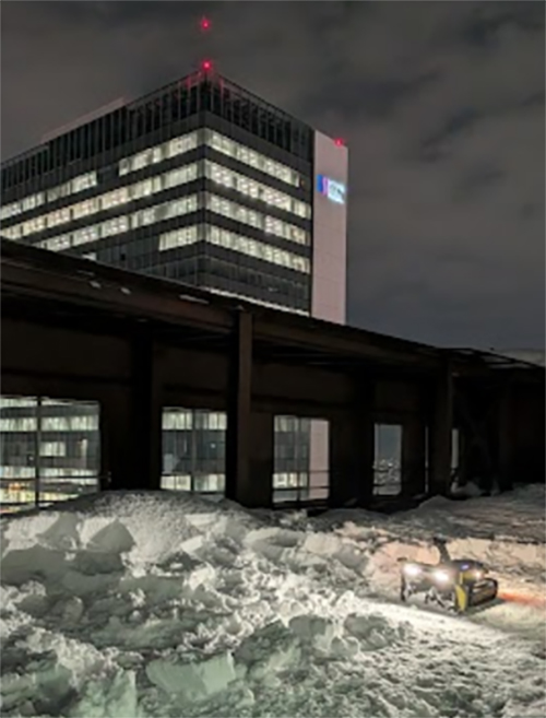札幌創世スクエアの前で自動除雪ロボットが除雪している様子。日が暮れてライトが点灯している。