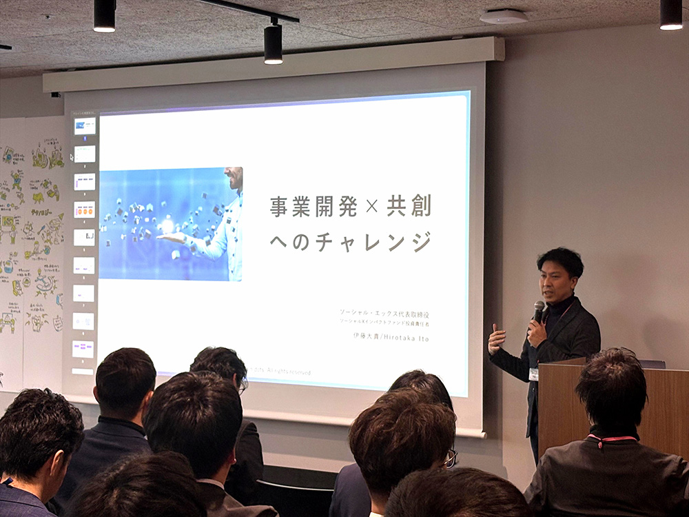 スクリーンに投影された「事業開発×共創へのチャレンジ」と伊藤氏