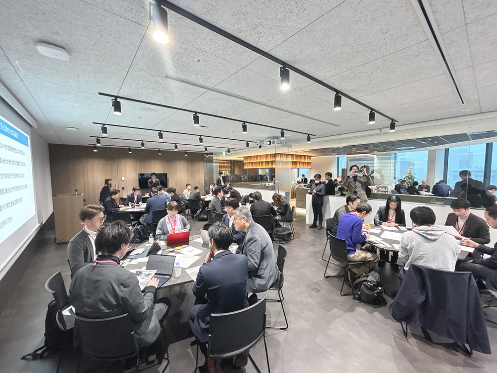 グループワークの様子。参加者がグループに分かれてテーブルを囲み、アイデア出しをしている引きの画像。