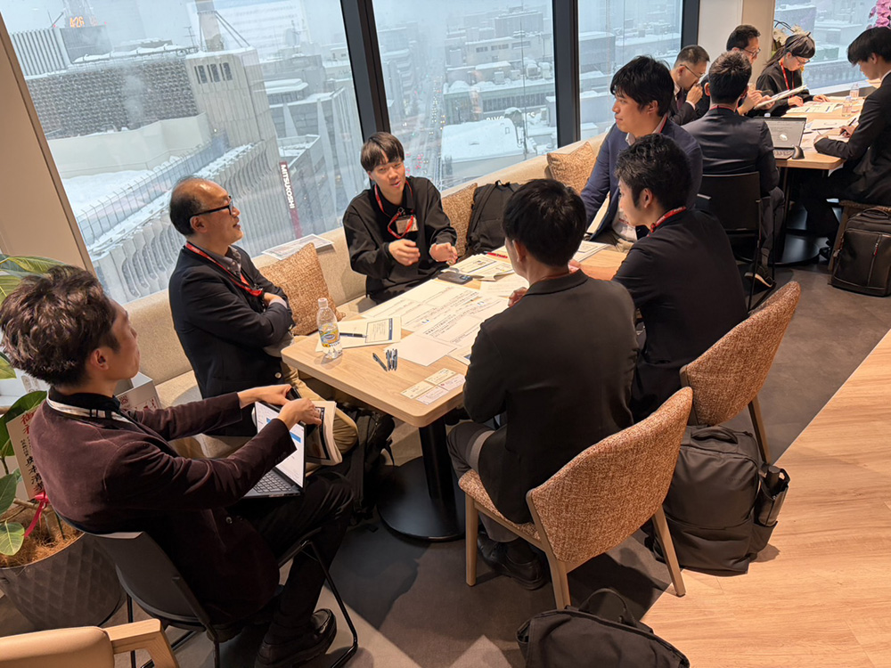 グループワークの様子。参加者がグループに分かれてテーブルを囲み、アイデア出しをしている寄りの画像。